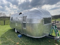 a silver airstream trailer is sitting on a grassy field