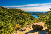 a rock on a cliff overlooking a lake and forest